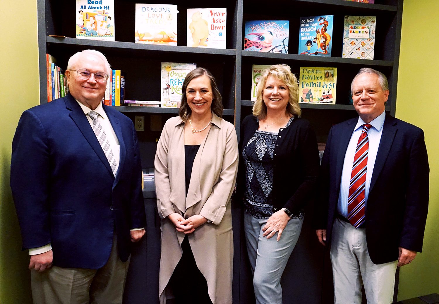 Four adults smiling in front of bookshelves